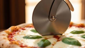 Pizzaskærer skærer gennem nybagt pizza med mozzarella og basilikum på rustikt træbræt